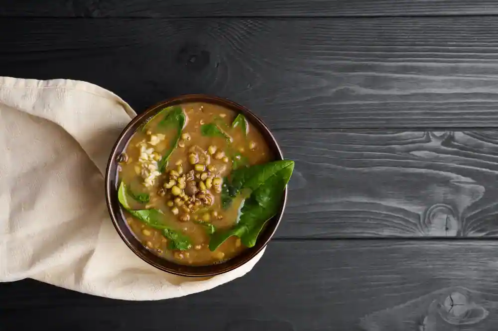 A bowl of Chainsoo (a traditional Uttarakhand lentil stew) garnished with fresh spinach leaves and grains, served on a dark wooden surface