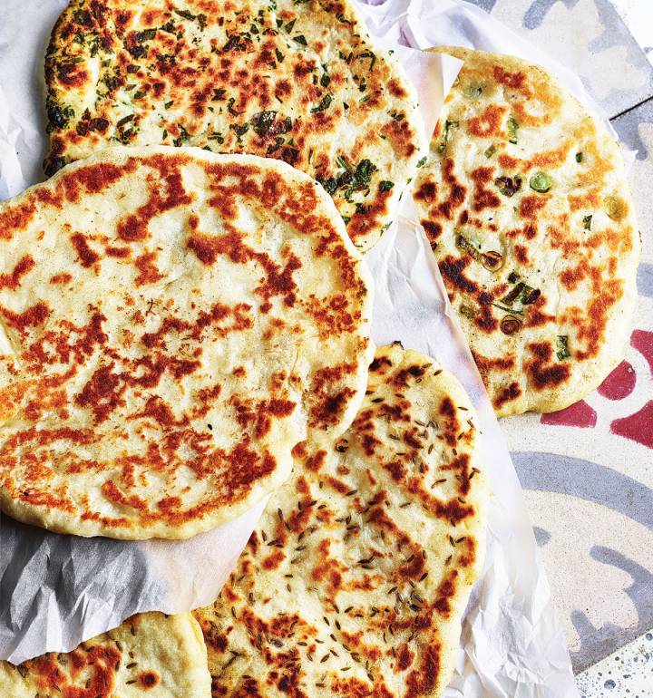 Rustic seeded flatbread resting on a soft linen cloth, placed on a textured stone countertop with natural soft daylight highlighting the golden-brown crust and scattered seeds.