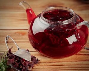 Rustic teapot steeping a garden-foraged herbal elixir, styled as a folkloric offering with rosemary and hibiscus, bathed in warm, moody light.